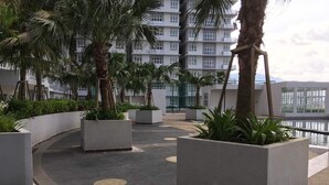 A rooftop terrace with planters and palm trees, overlooking a body of water and a building with balconies. - M3 Residences (Batu Caves)