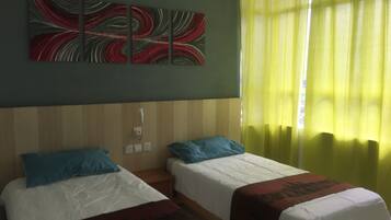 A hotel room with two single beds, a wall-mounted power outlet, and a window with yellow curtains.