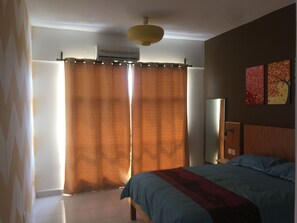 Un dormitorio con cama, mesita de noche, espejo y ventana con cortinas.