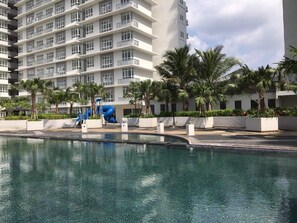 Una piscina con tobogán, rodeada de palmeras y un edificio de varios pisos con balcones.