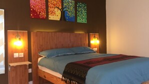 A bedroom with a wooden bed, blue bedding, and a colorful abstract painting above the bed. - M3 Residences (Batu Caves)