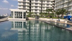 A swimming pool with clear water, surrounded by a modern building with multiple balconies and palm trees. - M3 Residences (Batu Caves)