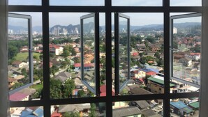 A view through a window with a grid pattern, displaying a cityscape with various buildings and greenery. - M3 Residences (Batu Caves)
