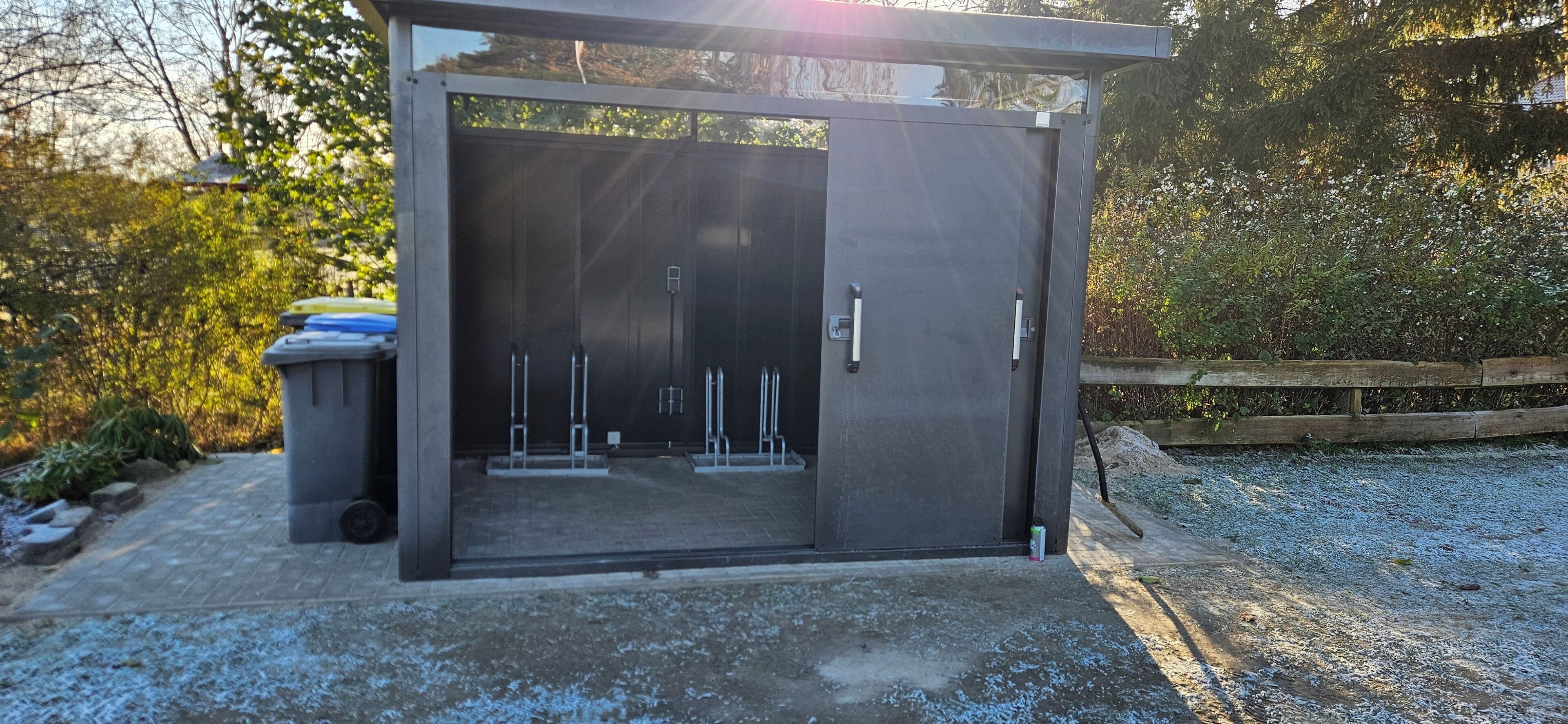 A modern, enclosed outdoor area with a metal door, a trash bin, and a gravel path.
