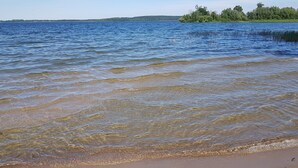A beach with clear water, a sandy shore, and a forested island in the background.