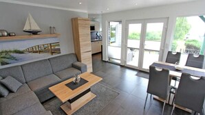 A modern living room with a grey sofa, a wooden coffee table, and a dining area with a table and chairs.