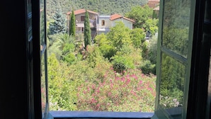 Blick durch ein offenes Fenster auf eine Berglandschaft mit Häusern und Grünflächen.