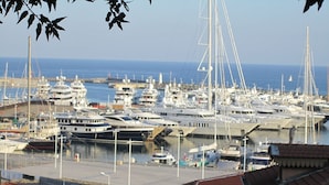Ein Yachthafen mit mehreren angossenen Yachten, freier Meeresblick und Gebäude im Vordergrund mit roten Ziegeldächern.