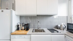 Moderni keittiö, jossa on valkoiset kaapit, ruostumattomasta teräksestä valmistettu pesuallas, kahvinkeitin, leivänpaahdin ja mikroaaltouuni.