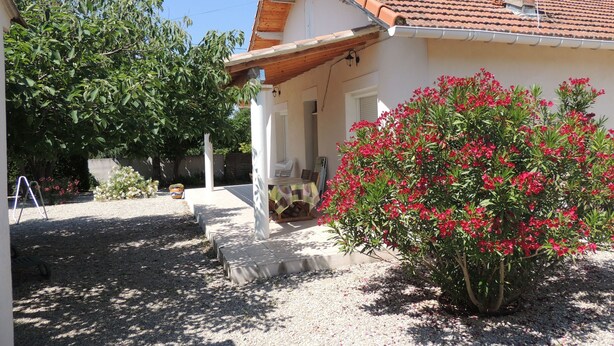 A house with a tiled roof, a porch, and a garden with red flowers.