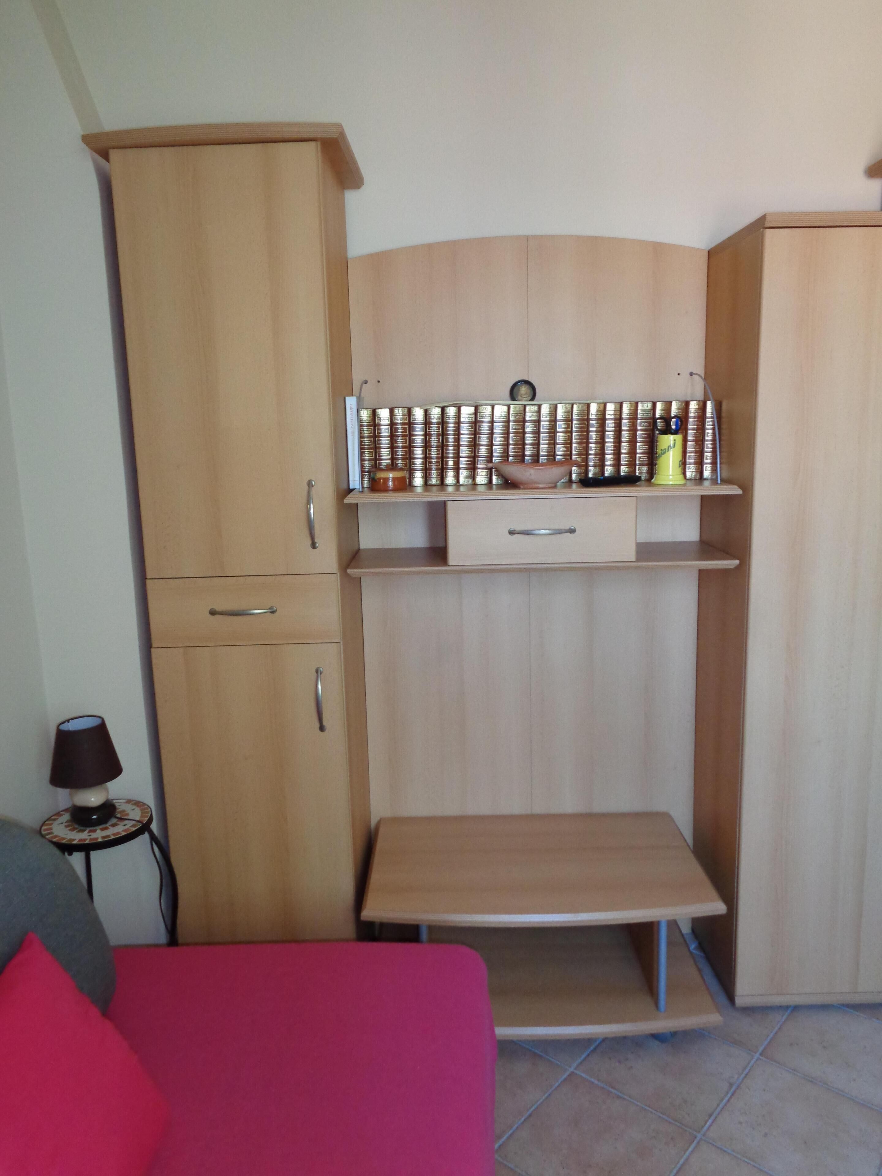 A compact room with a wooden cabinet, a small table, and a bed with a red cover.