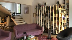 Moderni olohuone, jossa on violetti sohva, kirjahylly ja portaat, jotka johtavat ylemmälle tasolle.
