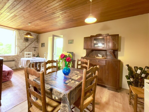 A dining area with a wooden table, chairs, a vase with flowers, and a cabinet with wine bottles.