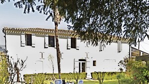 A white building with a tiled roof and a covered patio area. There is a table with chairs and a small garden with grass and a few plants. - Winetourism in the heart of Bordeaux (Margueron)
