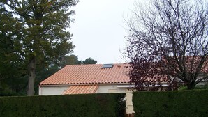 Una casa residencial con techo de tejas, una ventana pequeña y un seto recortado.