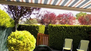 Un patio al aire libre con un toldo a rayas, una mesa con sillas y setos bien recortados.
