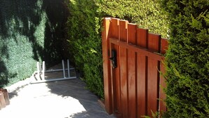 Una verja de madera con manija metálica, que da paso a un sendero rodeado de abundante follaje verde.