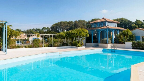Una piscina con superficie de agua azul cristalina, rodeada por una terraza blanca y una estructura de pabellón azul.
