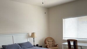 A bedroom with a bed, a desk, a chair, a ceiling fan, and a window with blinds. - Central Cedaredge Cottage (Cedaredge)