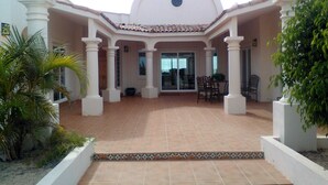Un’area patio coperta con pavimento piastrellato, colonne bianche e ingresso con porta in vetro.