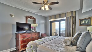 Hotelkamer met een bed, televisie, dressoir, plafondventilator en een raam met gordijnen.