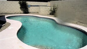 A swimming pool with a curved edge, surrounded by a light-colored tiled deck.