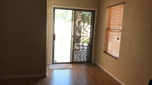 A room with a sliding glass door leading to an outdoor area, a window with blinds, and a wooden floor.