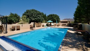 Une piscine rectangulaire, bordée d’une terrasse carrelée, entourée de chaises longues et de parasols.