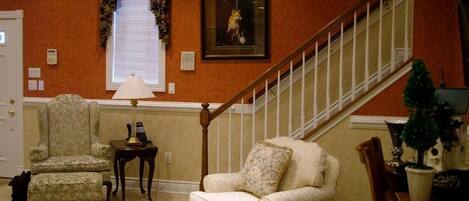 A living room with a staircase, a patterned armchair, a sofa, and a small table with a lamp.