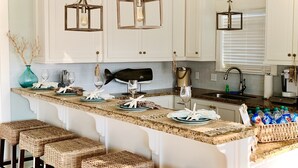 Una cocina con gabinetes blancos, una isla central con taburetes de bar, lámparas colgantes y una decoración con forma de pez.