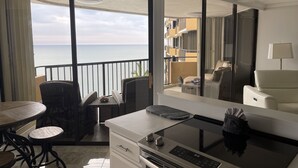 Una camera d'albergo moderna con un balcone vista mare, una zona pranzo con tavolo e sedie, e un grande specchio che riflette la stanza e il balcone.