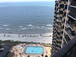 Un hotel moderno con vistas a una playa, piscina y sombrillas.