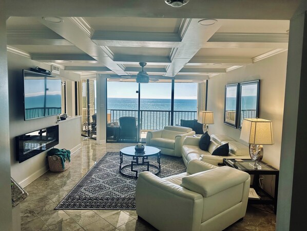 A spacious living room with a view of the sea, a ceiling fan, and a television.