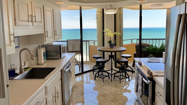 Una cucina moderna con vista sull'oceano, una zona pranzo con tavolo e sedie, e un balcone che si affaccia sul mare.