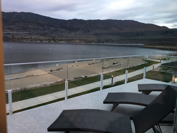 A balcony with outdoor seating overlooking a lake and mountains.