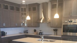Una cocina moderna con una isla central, taburetes de bar, electrodomésticos de acero inoxidable e iluminación colgante.