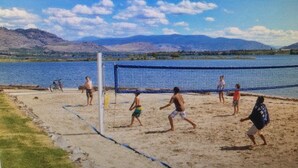 Partido de voleibol de playa con jugadores en primer plano y montañas al fondo.