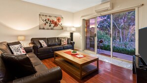 A living room with a sofa, coffee table, and a painting on the wall. - Bulla Hill Villas- Melbourne Airport (Bulla)