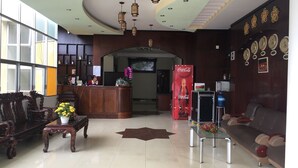 A reception area with a wooden reception desk, a Coca-Cola refrigerator, a sofa, and a decorative wall with clocks. - Memories Hotel (B'Lao)
