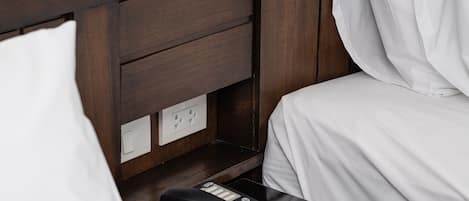 A hotel room with a wooden headboard, a bedside table with a telephone, and white bedding.