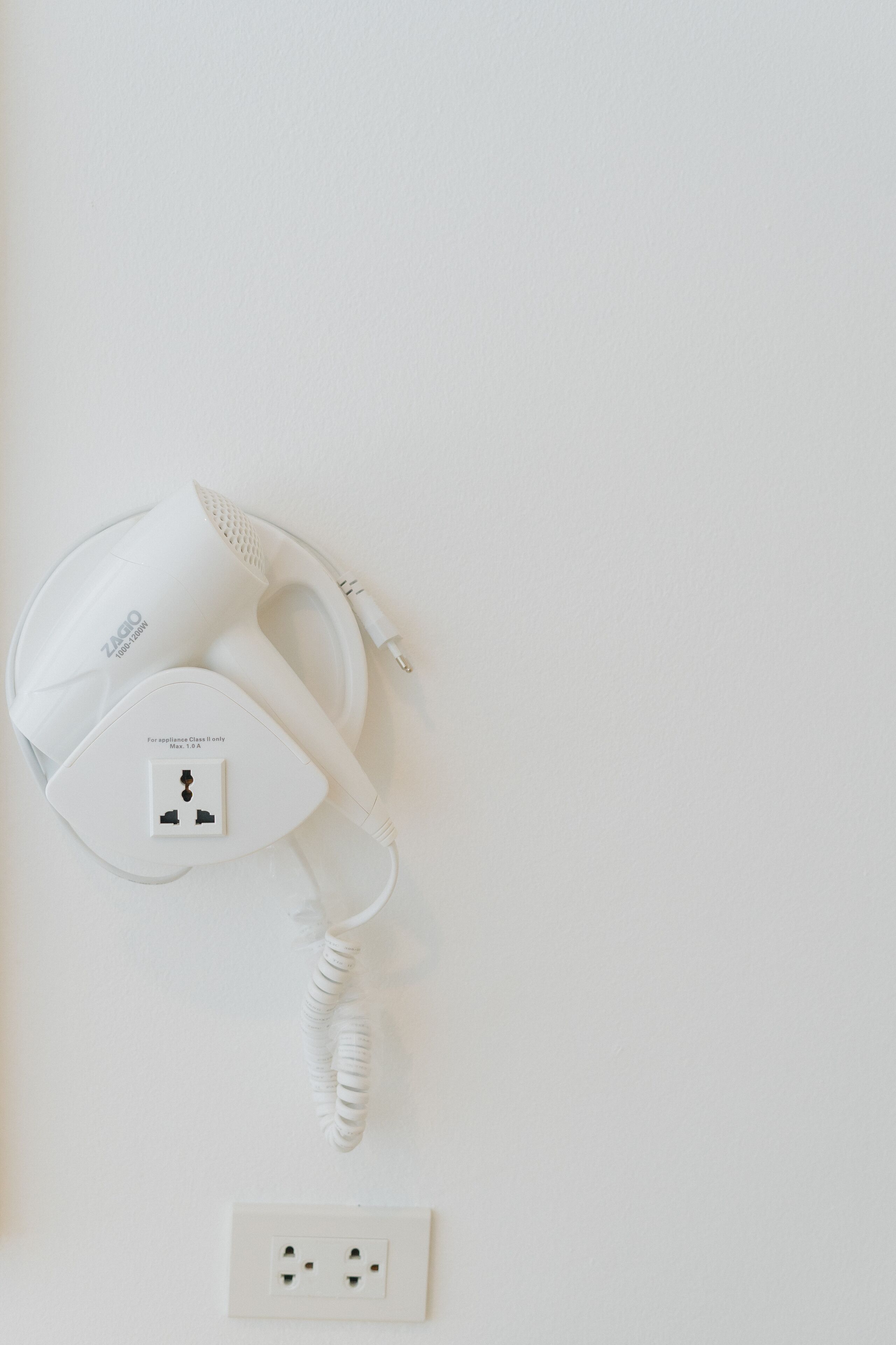 Un sèche-cheveux blanc, avec un câble branché dans une prise de courant.