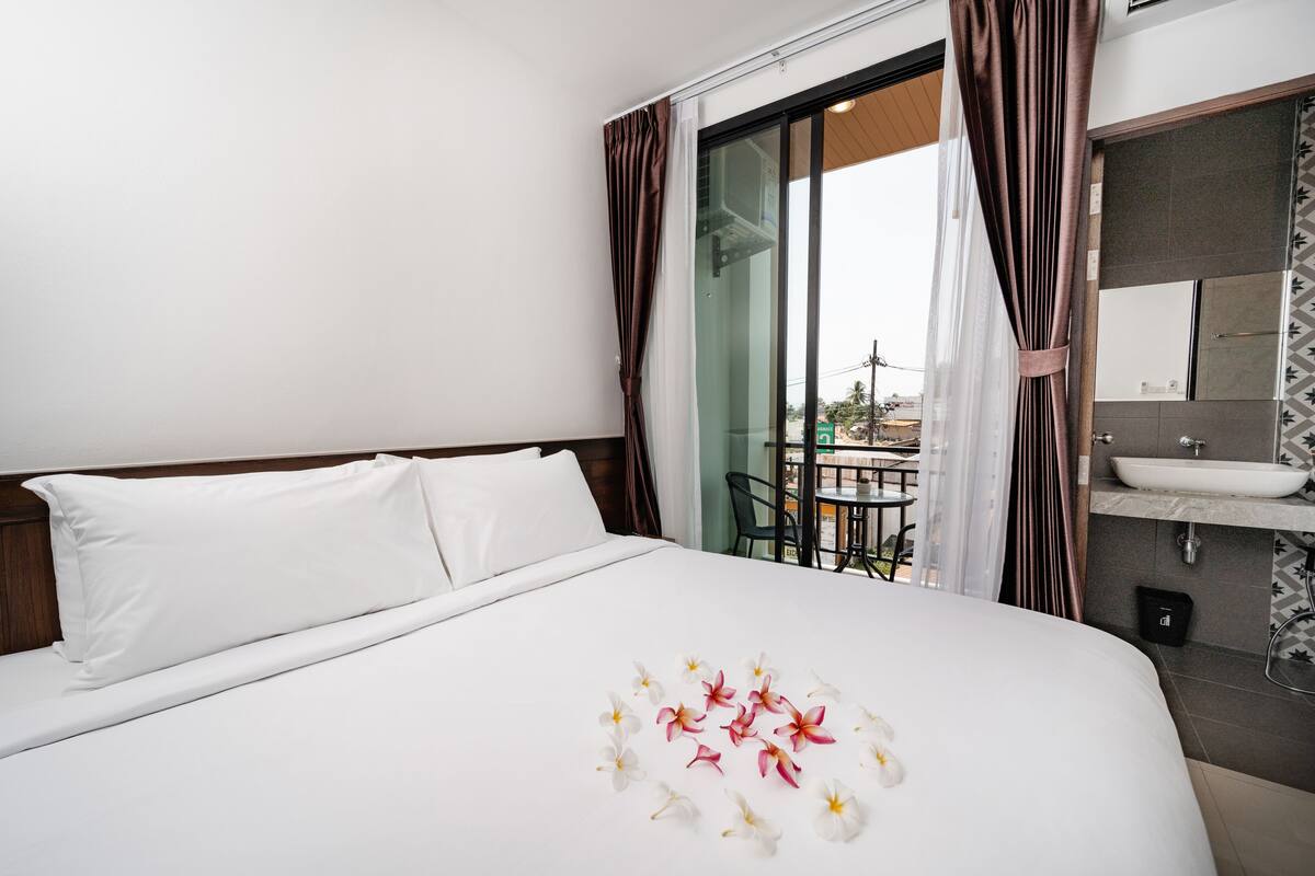 A hotel room with a large bed, a bathroom with a sink and mirror, and a balcony with a table and chairs.