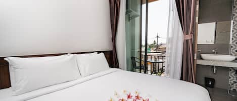A hotel room with a large bed, a bathroom with a sink and mirror, and a balcony with a table and chairs.