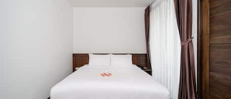 Una cama bien hecha con una colcha blanca y un arreglo floral, un cabecero de madera, una mesita de noche con una lámpara y una puerta de madera grande.