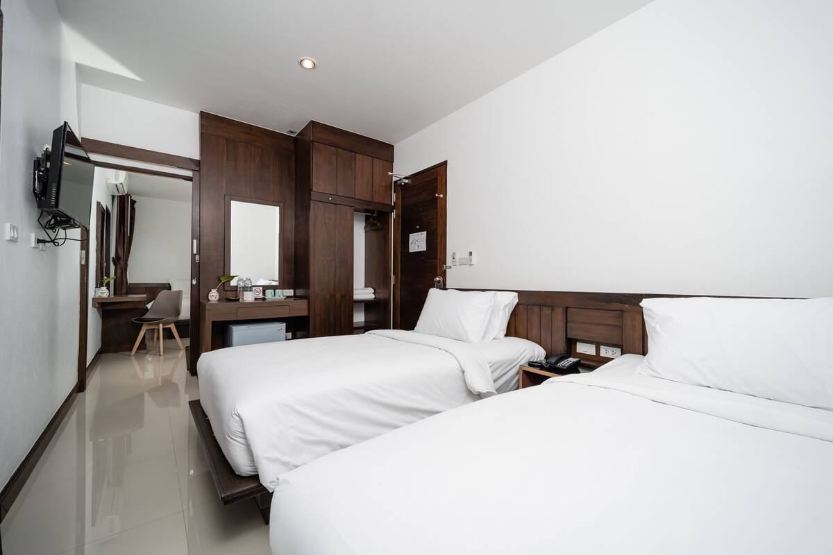 A hotel room with two beds, a desk, a chair, a wardrobe, and a mirror.