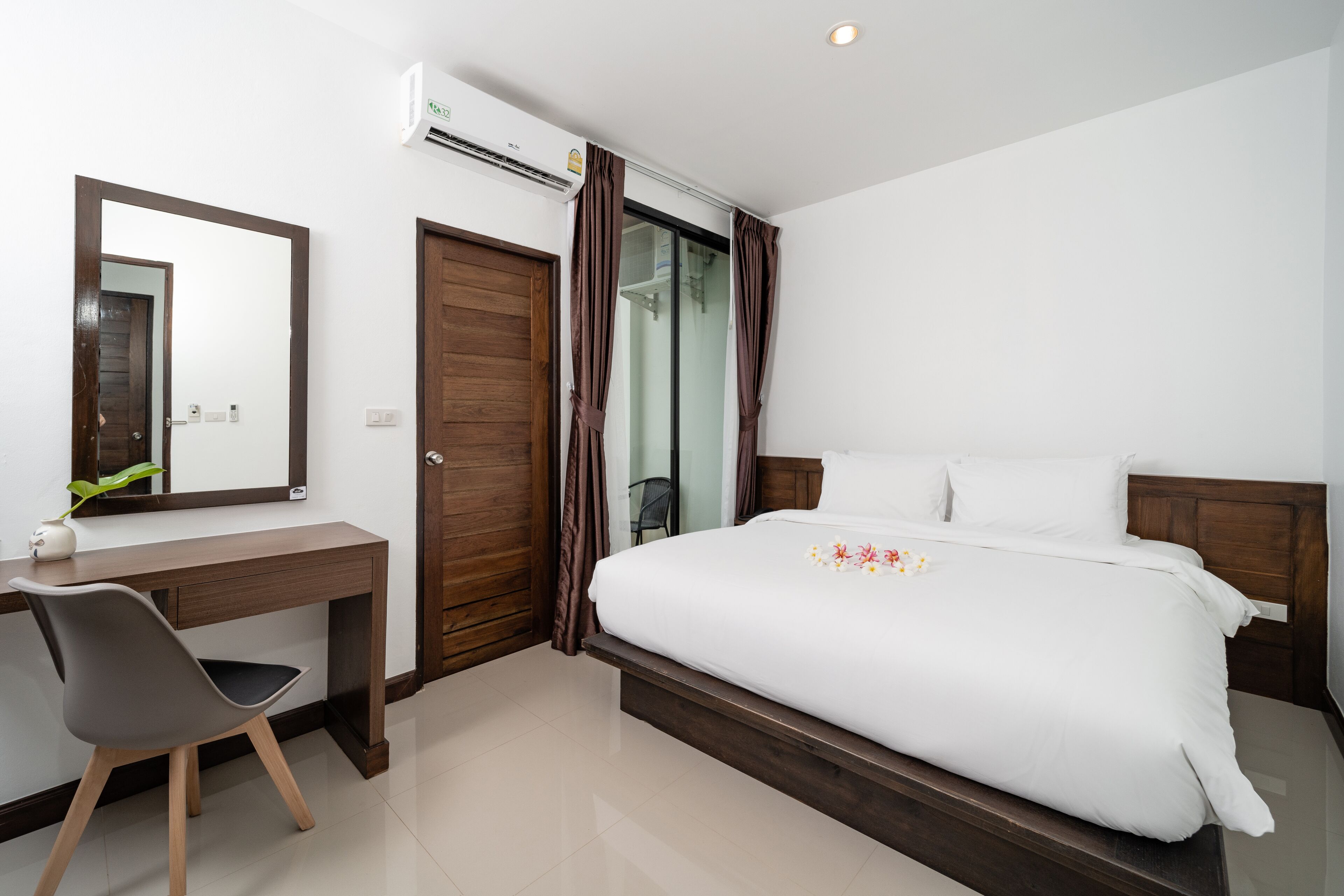 A bedroom with a bed, a desk, a chair, a mirror, and an air conditioning unit.