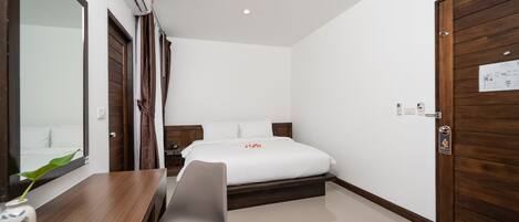 Ein Hotelzimmer mit Bett, Schreibtisch mit Stuhl, Spiegel und Holztür.