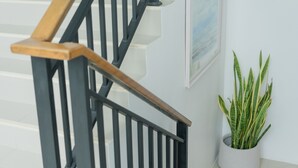 A staircase with a wooden handrail and black balusters, a potted plant, and a framed picture on the wall. - Circle Inn Ao Nam Mao (Krabi)