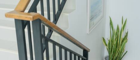 A staircase with a wooden handrail and black balusters, a potted plant, and a framed picture on the wall.