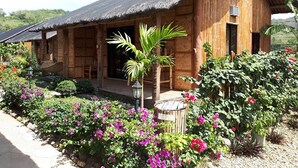 Un edificio de madera con techo de paja, rodeado de un jardín con diversas plantas y flores.